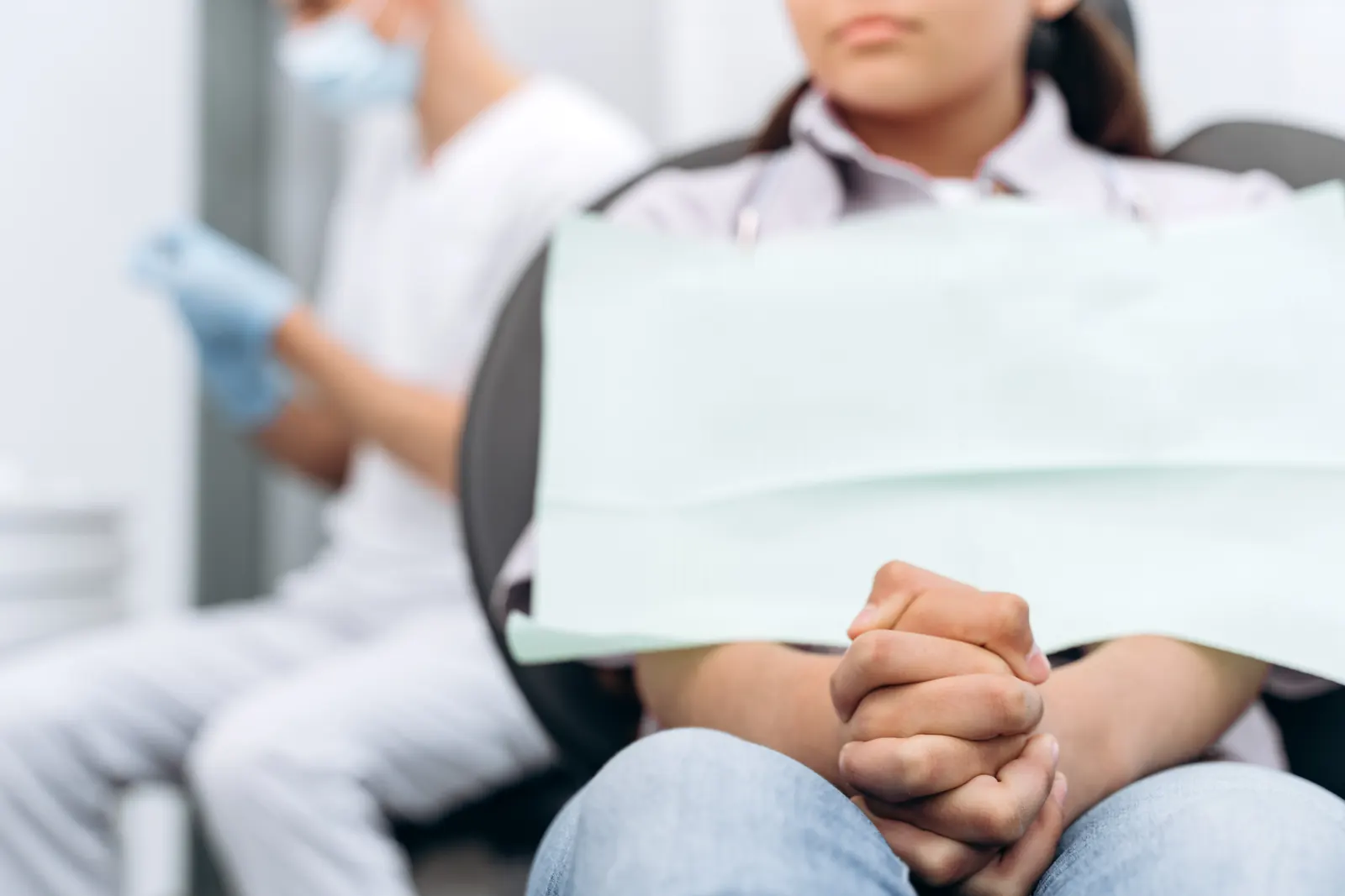 Gefaltete Hände im Behandlungsstuhl Patient mit gefalteten Händen im Behandlungsstuhl, im Hintergrund der Zahnarzt